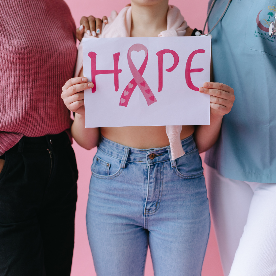  Three women together, one holding a paper with text promoting metastatic breast cancer awareness and support.