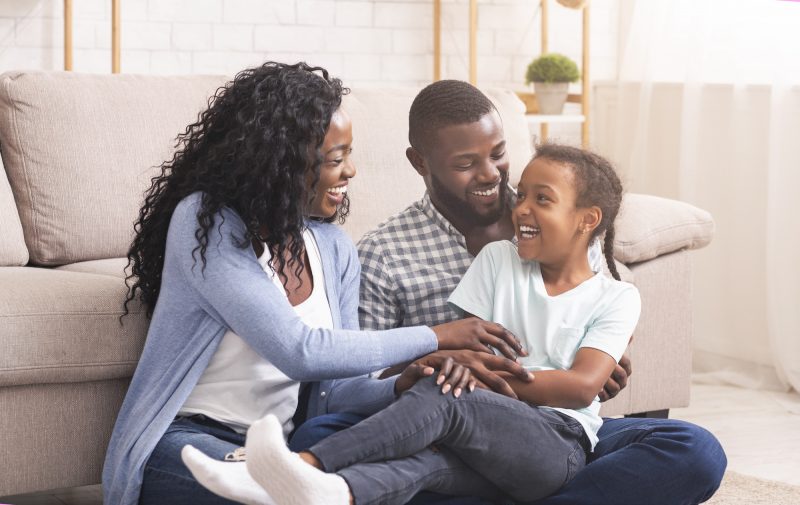 Smiling African American family with mother, father, and young son sitting together on a couch, illustrating successful co-parenting boundaries and harmonious family relationships.