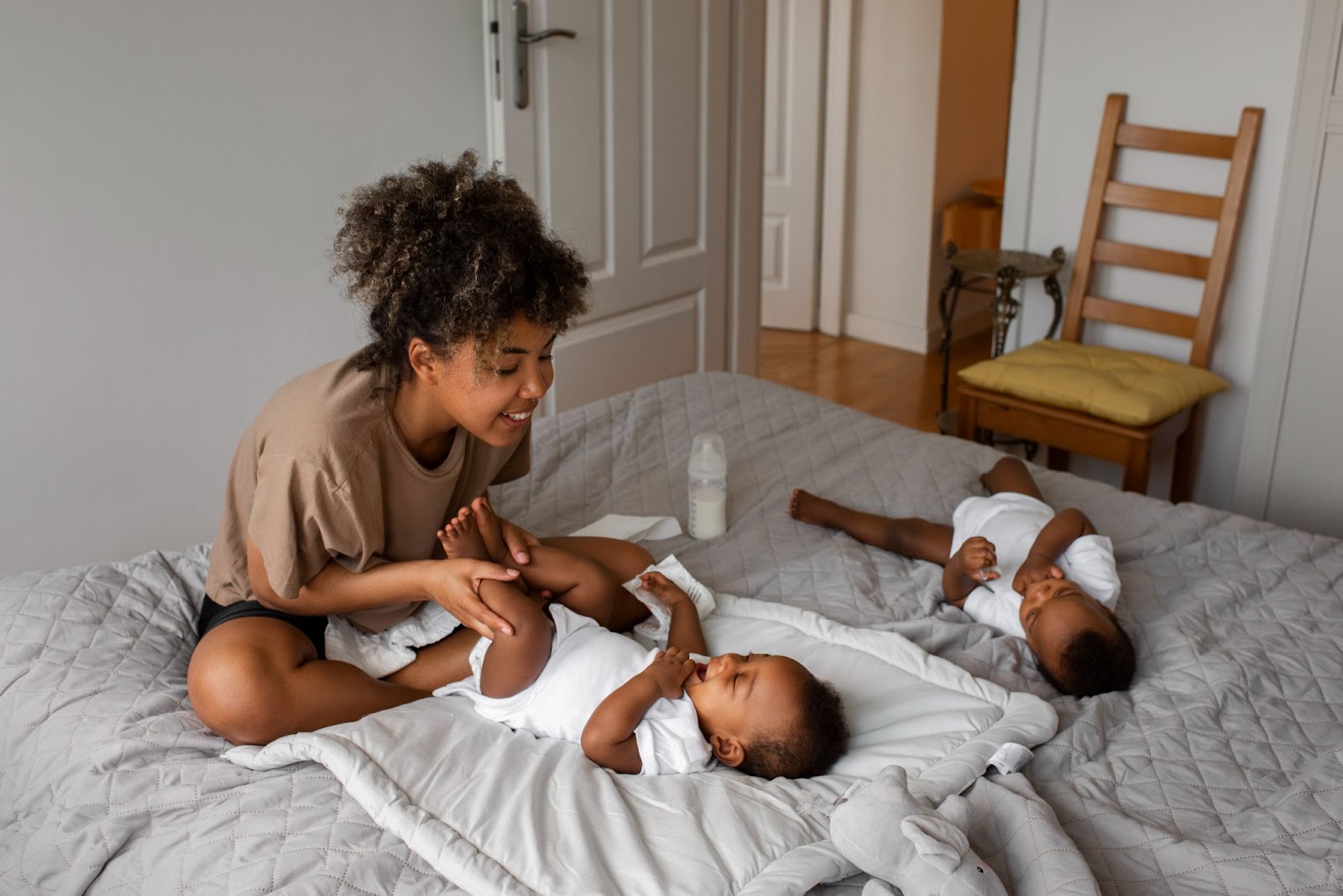 A smiling mother plays with her baby while another baby lies nearby — a candid scene that highlights self-care tips for new moms, showing how small, joyful moments can ease the stress of early motherhood.