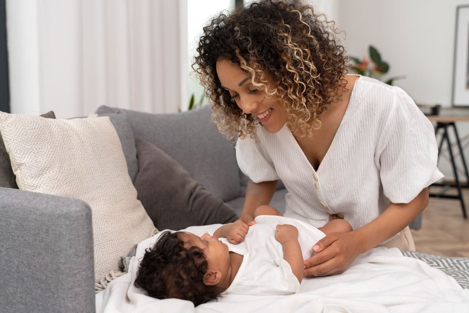 A joyful new mom smiles warmly at her baby while bonding on the couch—a heartwarming moment that reflects self-care tips for new moms, such as creating time for emotional connection and presence.