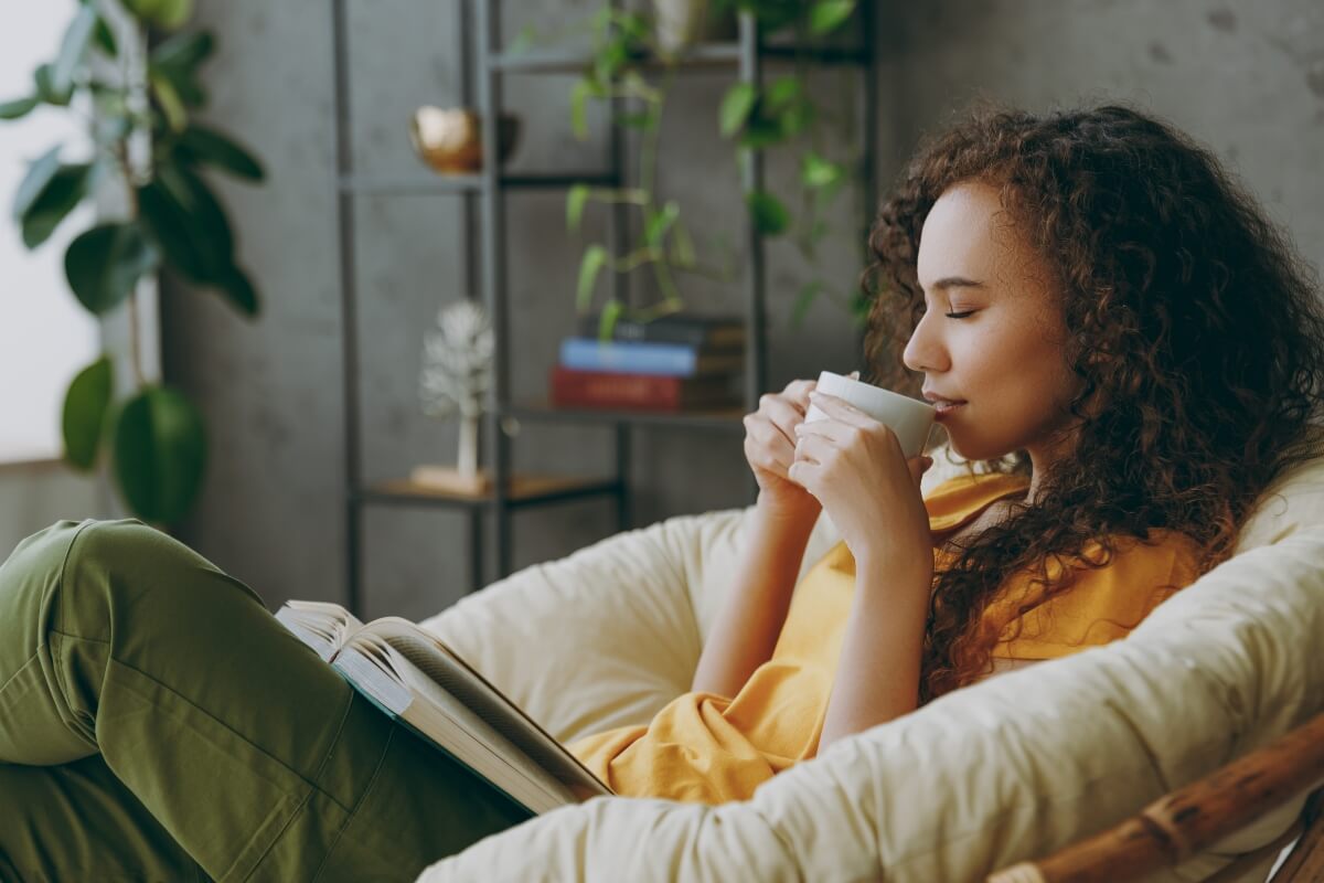 Woman relaxing with tea and book demonstrating self-care tips for new moms to reduce stress and exhaustion.